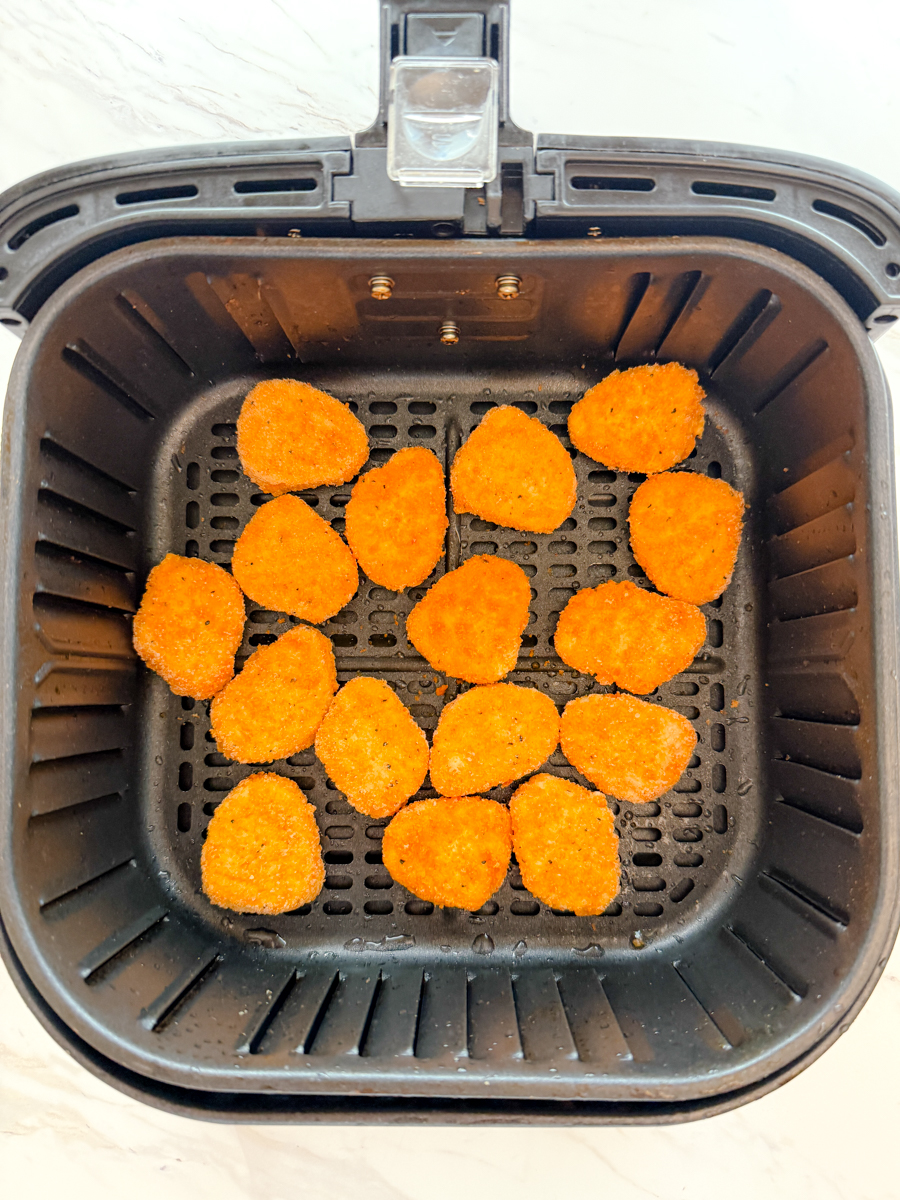 Overhead view of an air fryer basket with chicken nuggets in it.