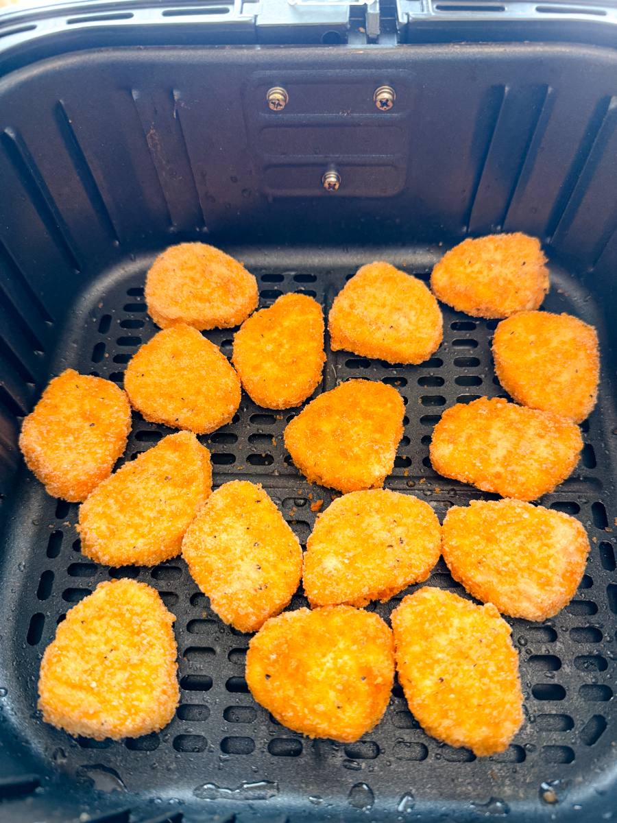Angled view of an air fryer basket with chicken nuggets in it.