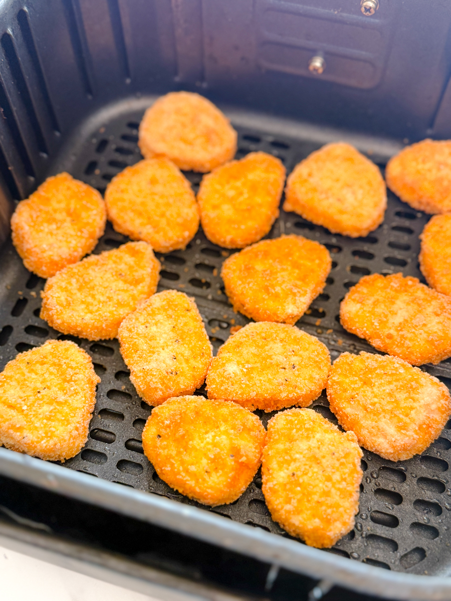 Angled view of an air fryer basket with chicken nuggets in it.