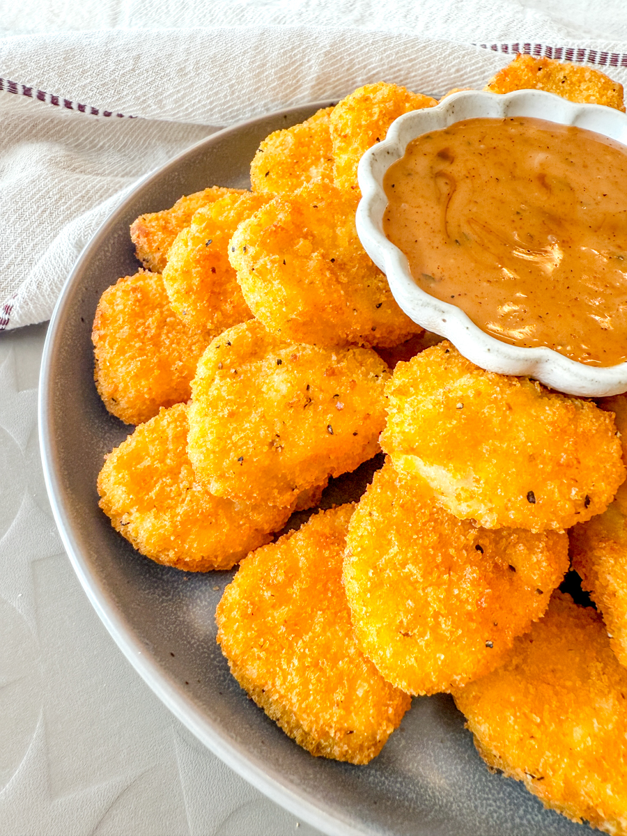 Angled view of a plate of Air Fryer Frozen Chicken Nuggets with a dipping sauce.