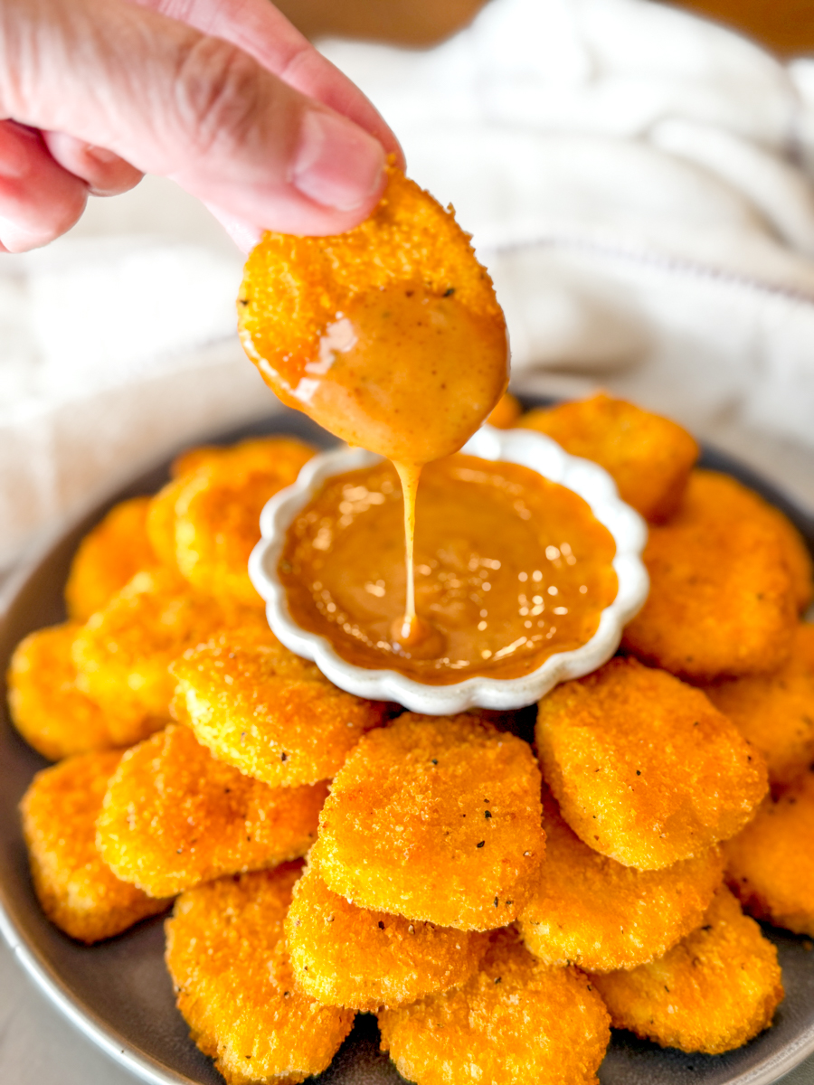 Angled view of a hand dipping a chicken nugget into a dipping sauce on a plate of Air Fryer Frozen Chicken Nuggets.