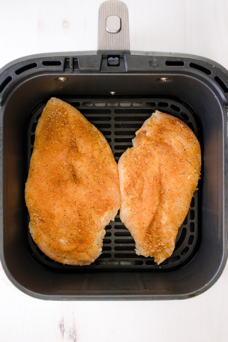 Overhead view of seasoned raw chicken breasts in an air fryer basket.