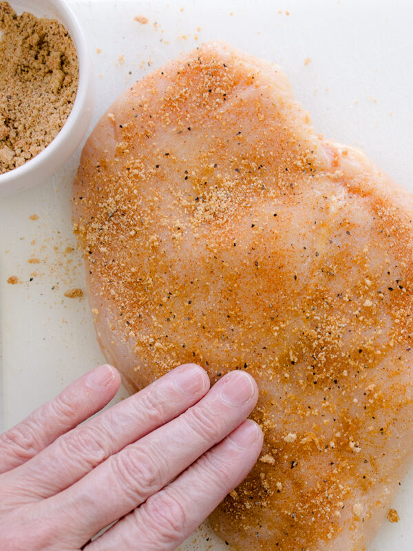 Overhead view of a hand rubbing seasoning into raw chicken breasts.