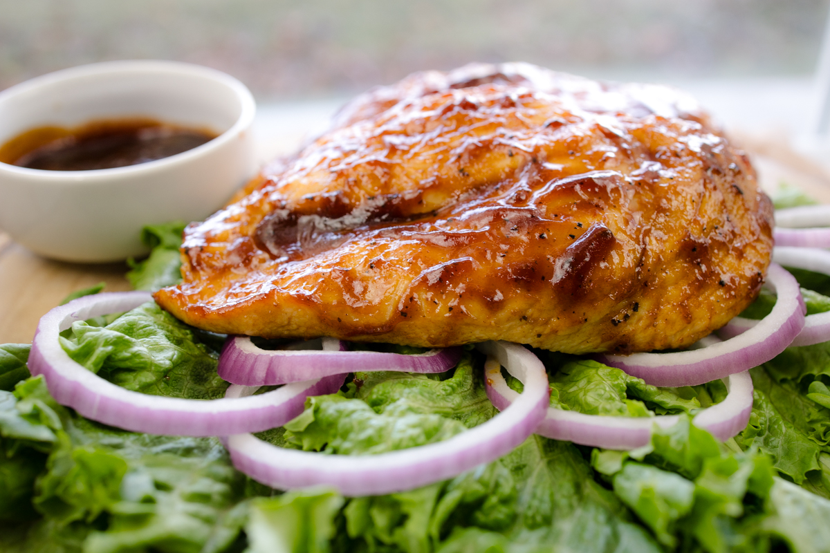 Side view of Air Fryer BBQ Chicken on a bed of salad next to some BBQ sauce in a white ramekin.