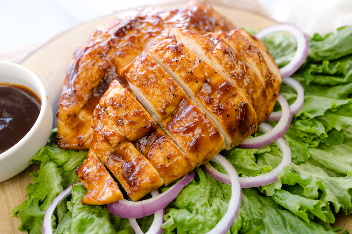 Angled view of Air Fryer BBQ Chicken on a bed of salad next to some BBQ sauce in a white ramekin.