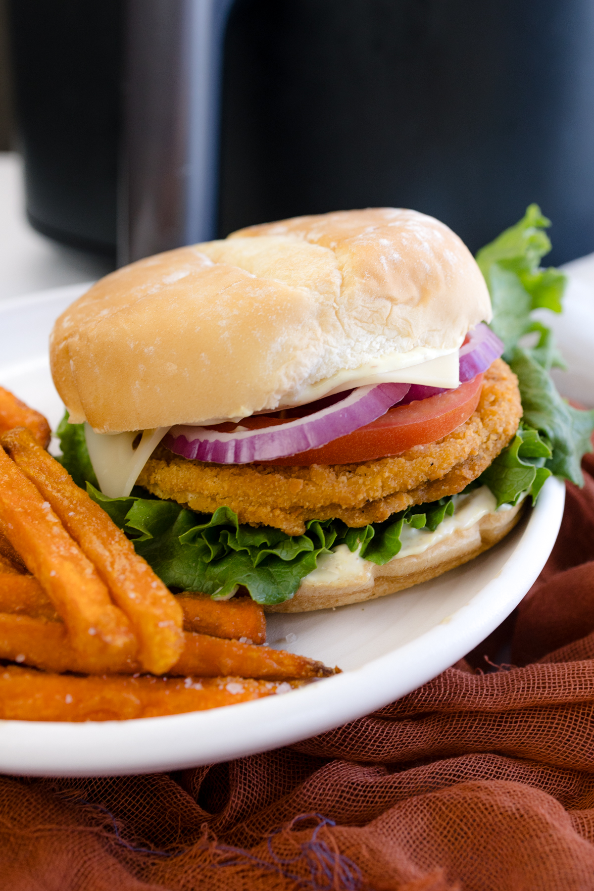 Angled image of a chicken patty sandwich on a plate with sweet potato fries.