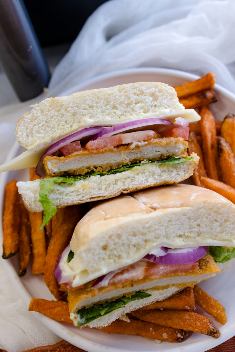 Angled image of a chicken patty sandwich on a plate with sweet potato fries.