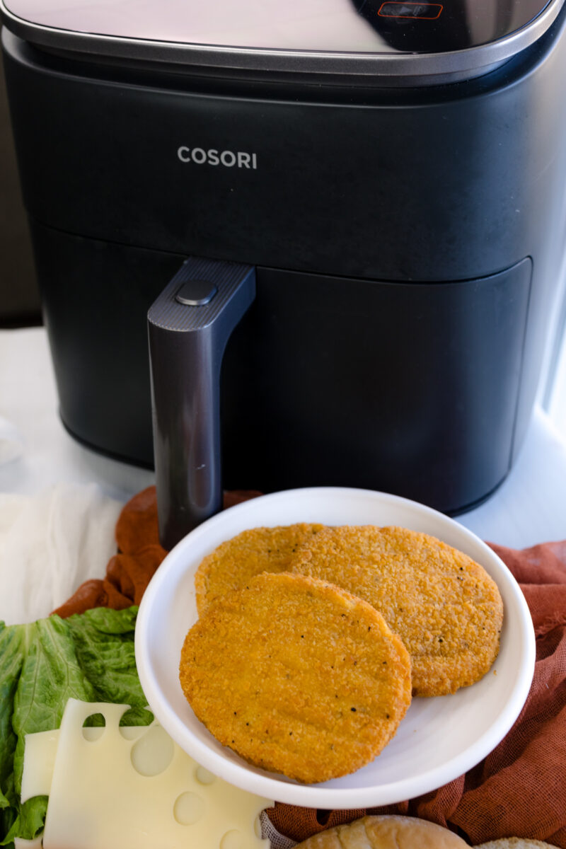Close up image of all ingredients and toppings for making chicken patty sandwiches, next to an air fryer.