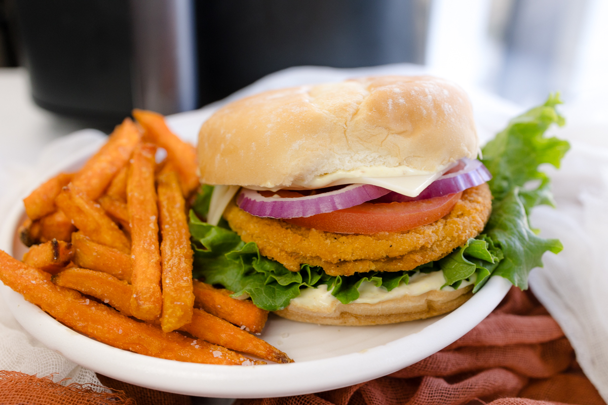 Angled image of a chicken patty sandwich on a plate with sweet potato fries.