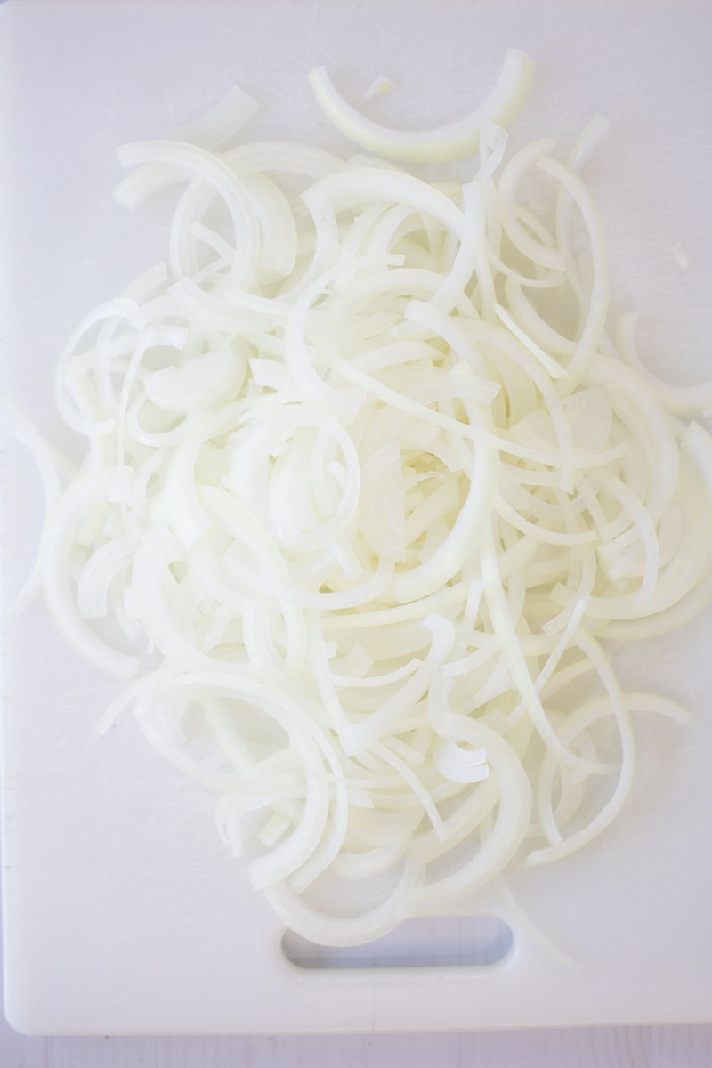 Overhead view of raw onion slices on a chopping board.