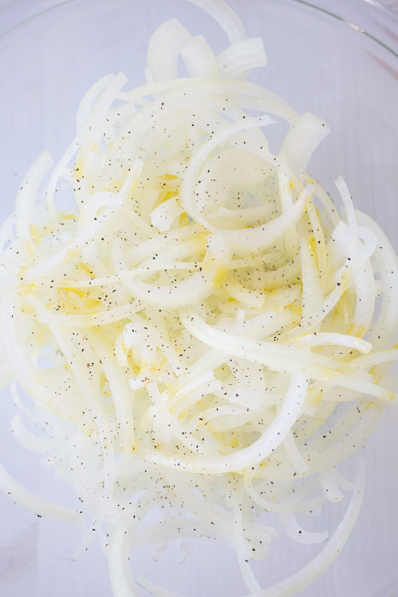 Overhead view of seasoned raw onion slices on a chopping board.
