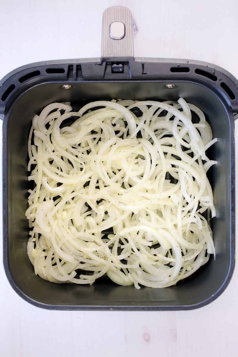 Overhead view of raw onion slices in an air fryer basket.
