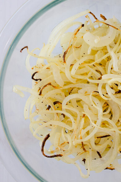 Overhead view of an onion next to a glass bowl of air fryer onions.