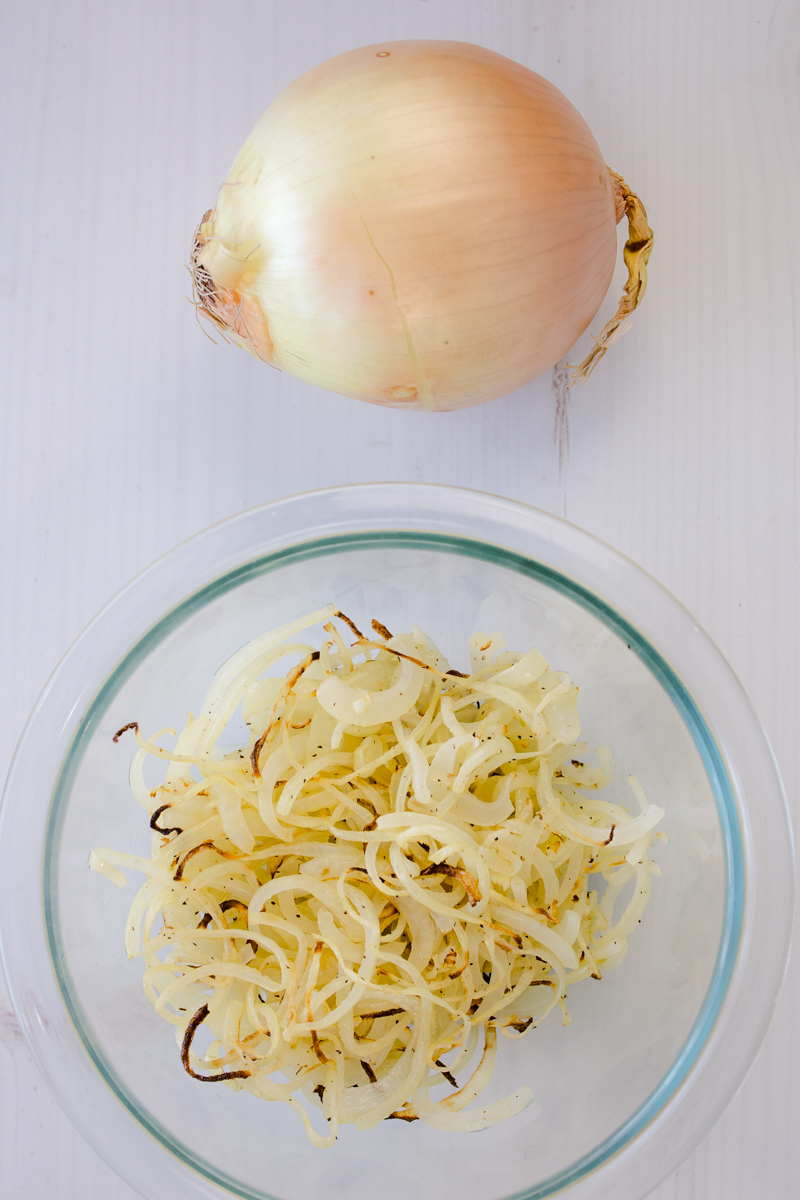 Overhead view of an onion next to a glass bowl of air fryer onions.