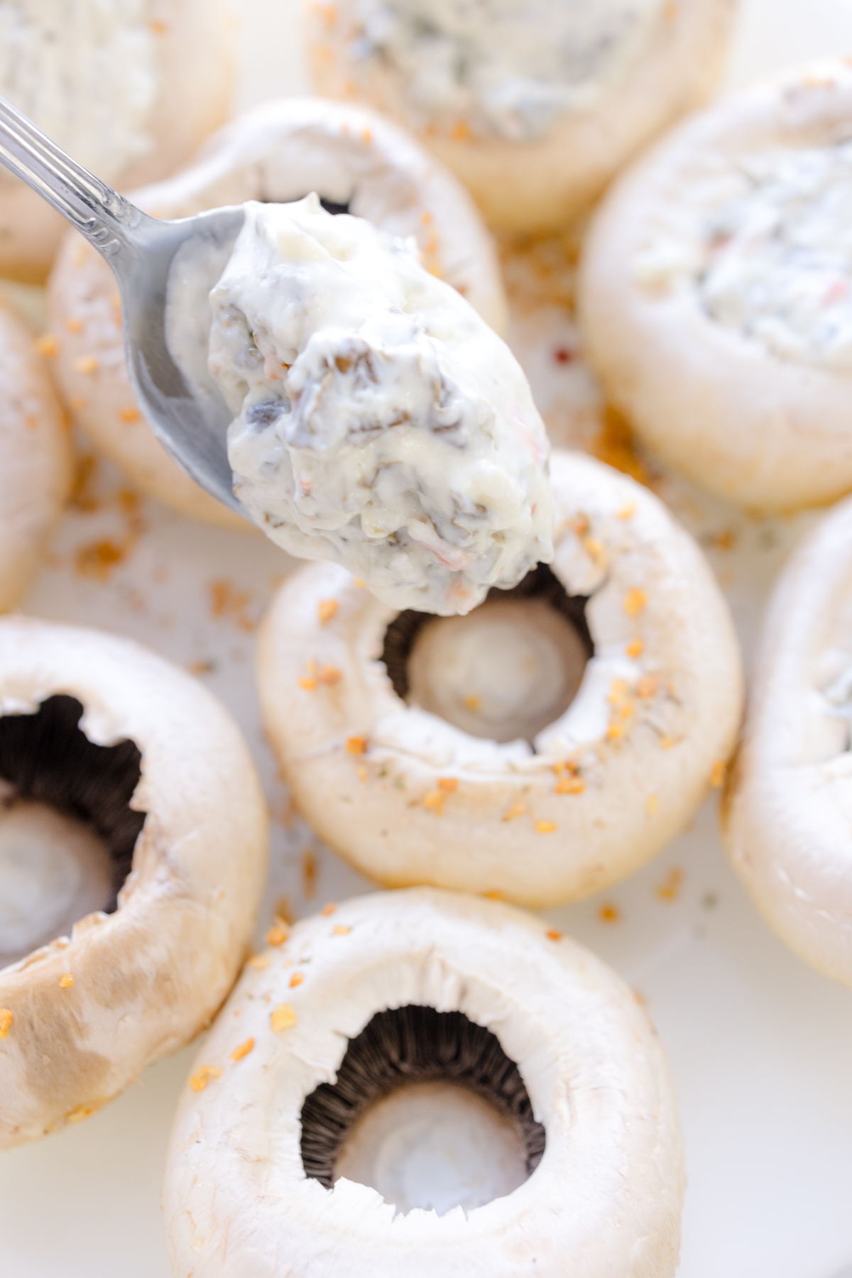Close up image of mushrooms being filled with spinach artichoke dip.