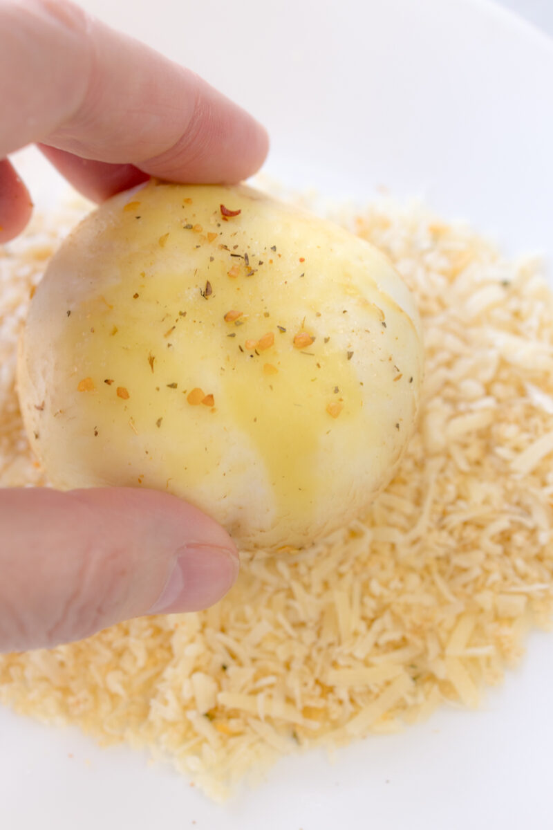 Close up image of a mushroom being coated with Parmesan & Panko breadcrumbs.
