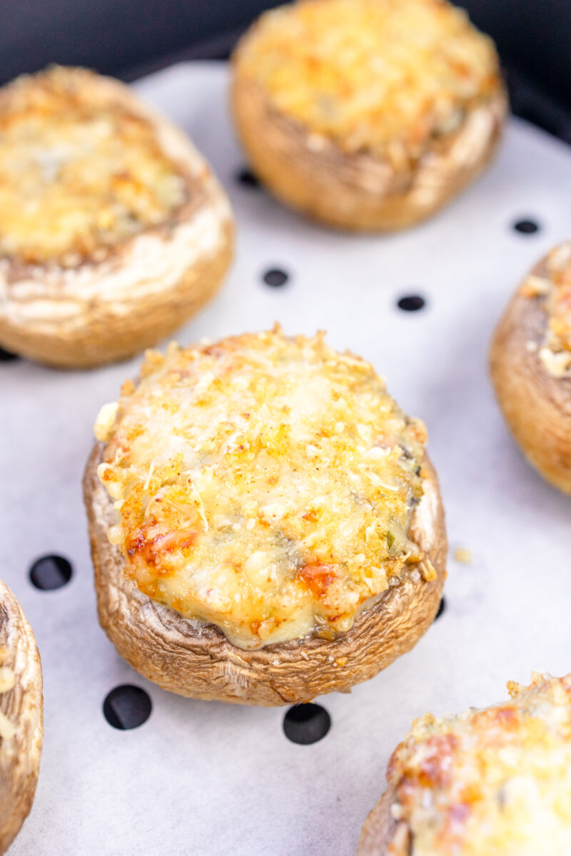 Close up image of Air Fryer Stuffed Mushrooms in an air fryer basket lined with parchment paper.