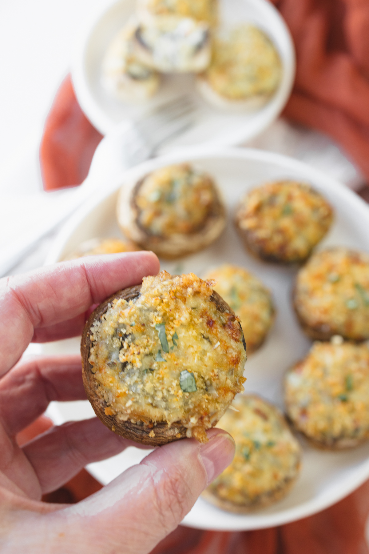 Close up image of a hand holding an Air Fryer Stuffed Mushroom over a plate of them.