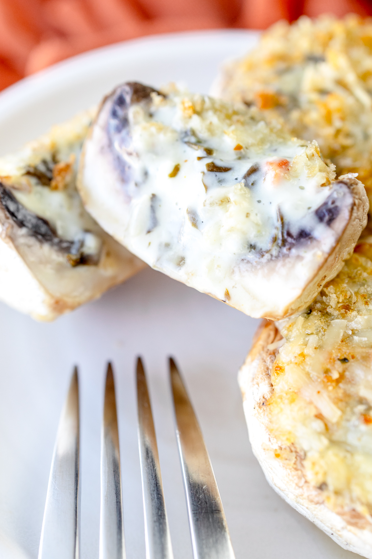 Close up image of Air Fryer Stuffed Mushrooms on a white plate with a fork. One mushroom is sliced in half to reveal the middle.