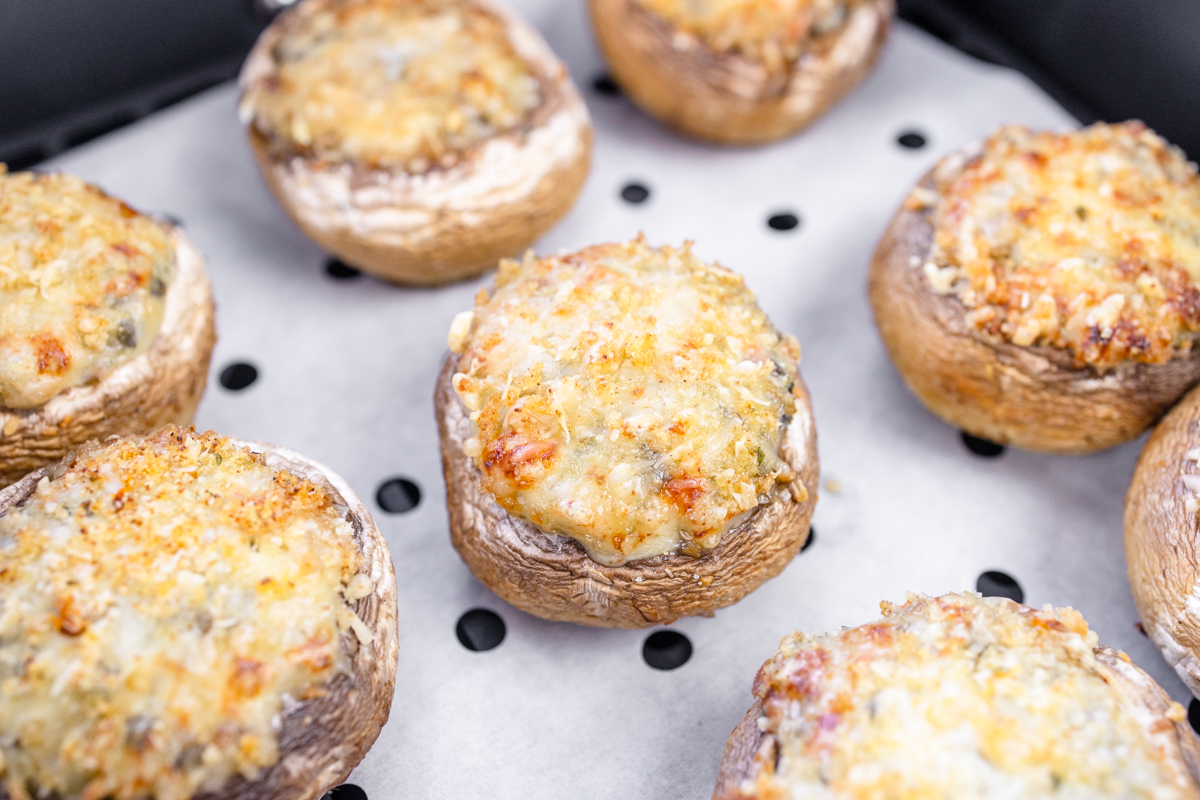 Close up image of Air Fryer Stuffed Mushrooms in an air fryer basket lined with parchment paper.