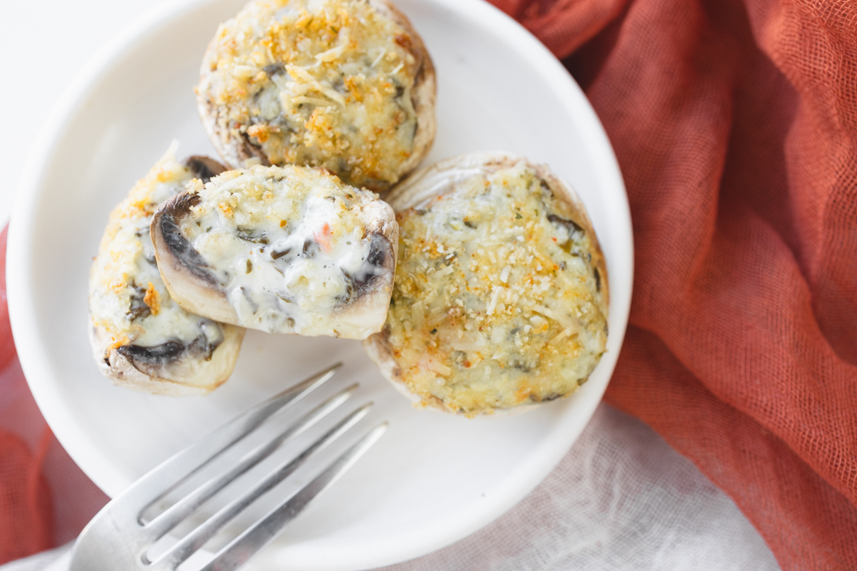Overhead image of Air Fryer Stuffed Mushrooms on a white plate with a fork. One mushroom is sliced in half to reveal the middle.