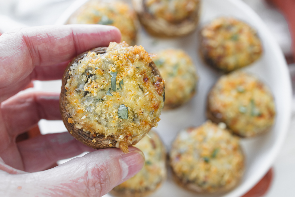Close up image of a hand holding an Air Fryer Stuffed Mushroom over a plate of them.