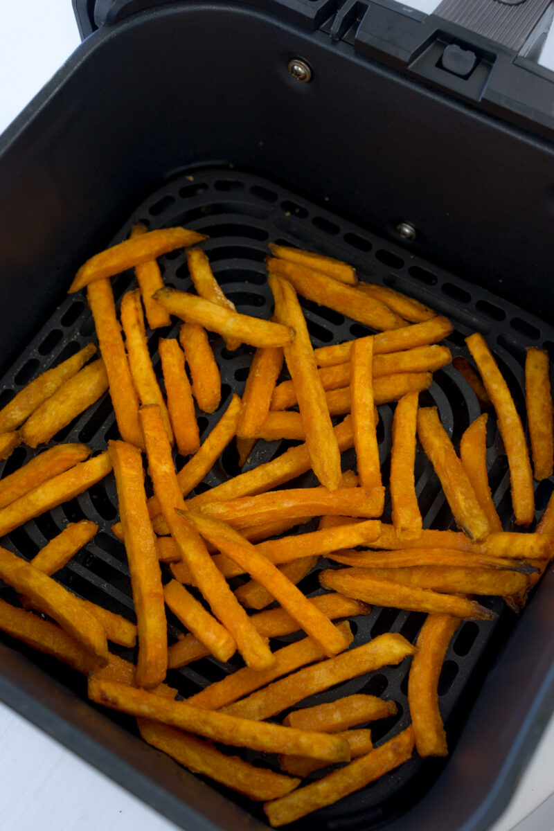 Angled view of sweet potato fries in an air fryer basket.