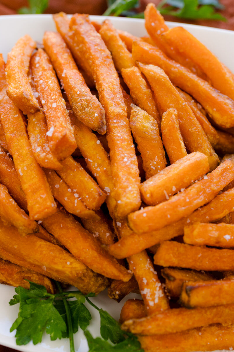 Close-up view of air fried sweet potato fries on a white serving platter.
