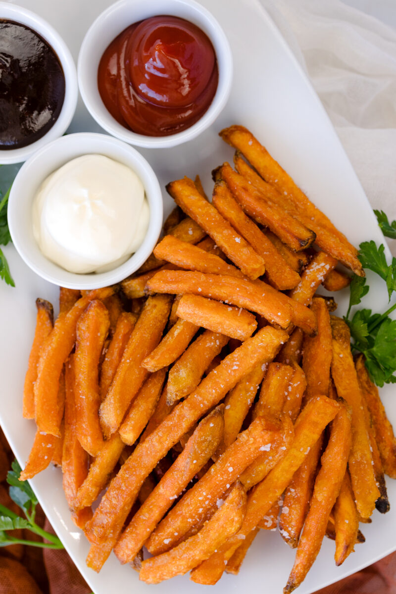 Overhead view of air fried sweet potato fries on a white serving platter with dipping sauces.