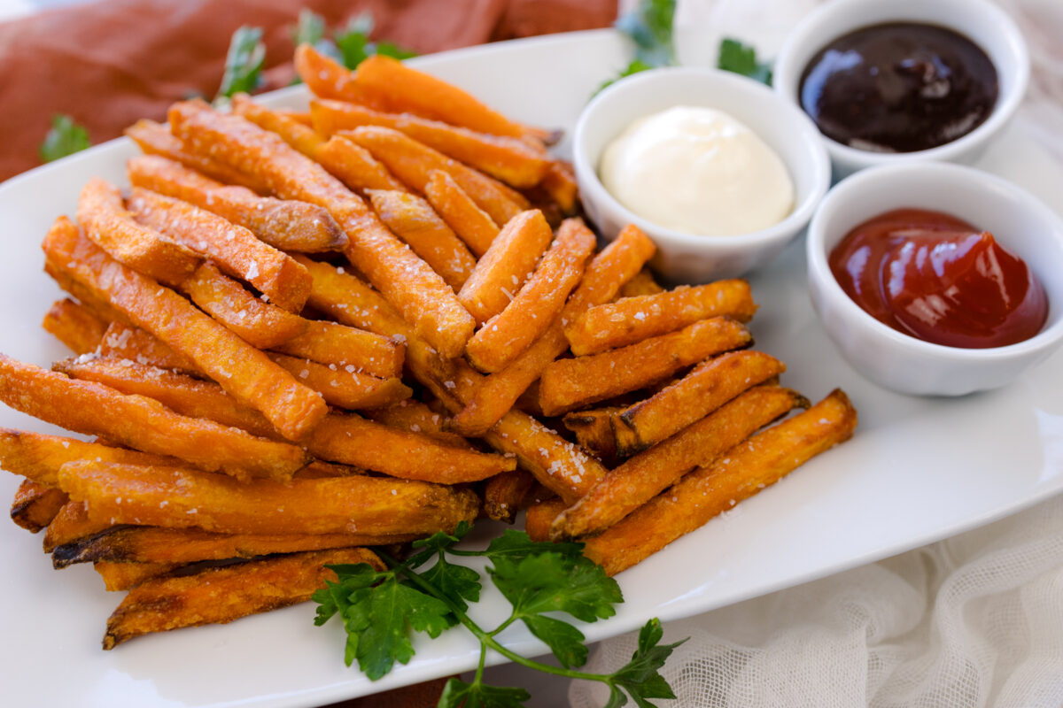 Angled view of air fried sweet potato fries on a white serving platter with dipping sauces.