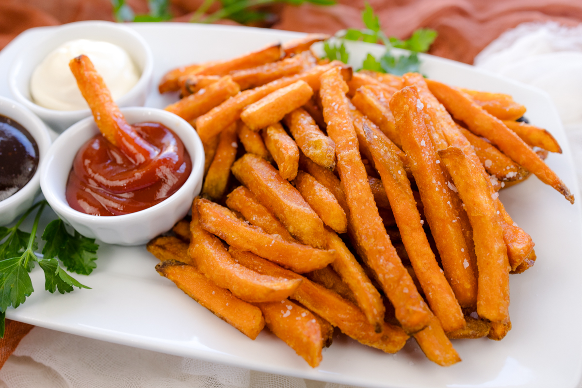 Angled view of air fried sweet potato fries on a white serving platter with dipping sauces.