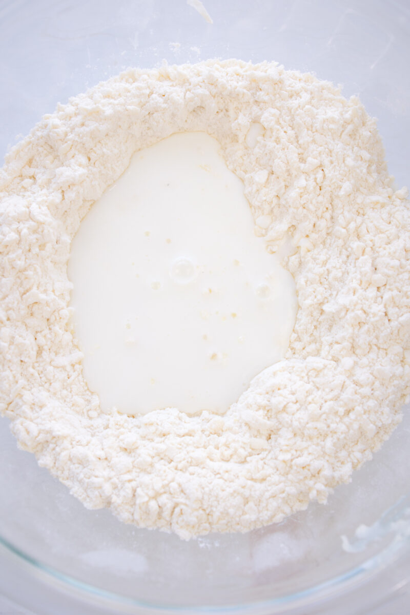 Pverhead view of buttermilk being added to the biscuit dough.