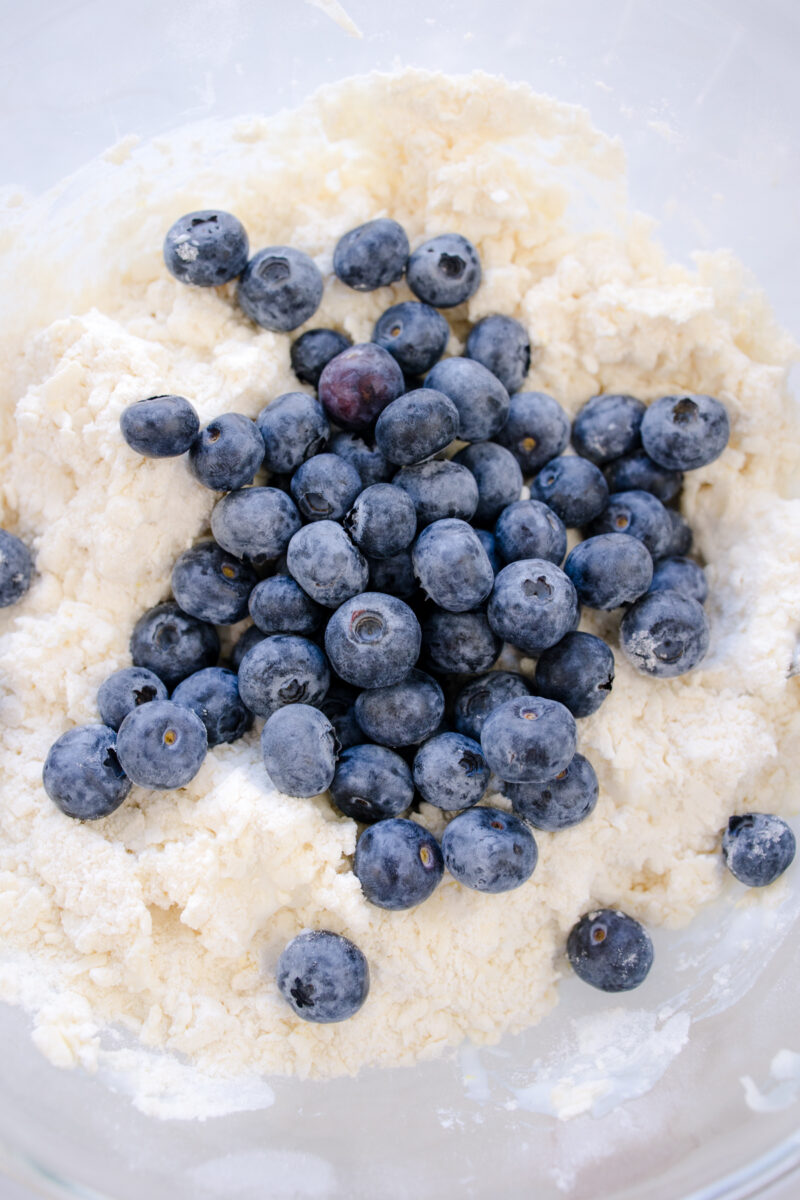 Overhead view of blueberries being added to the biscuit dough.