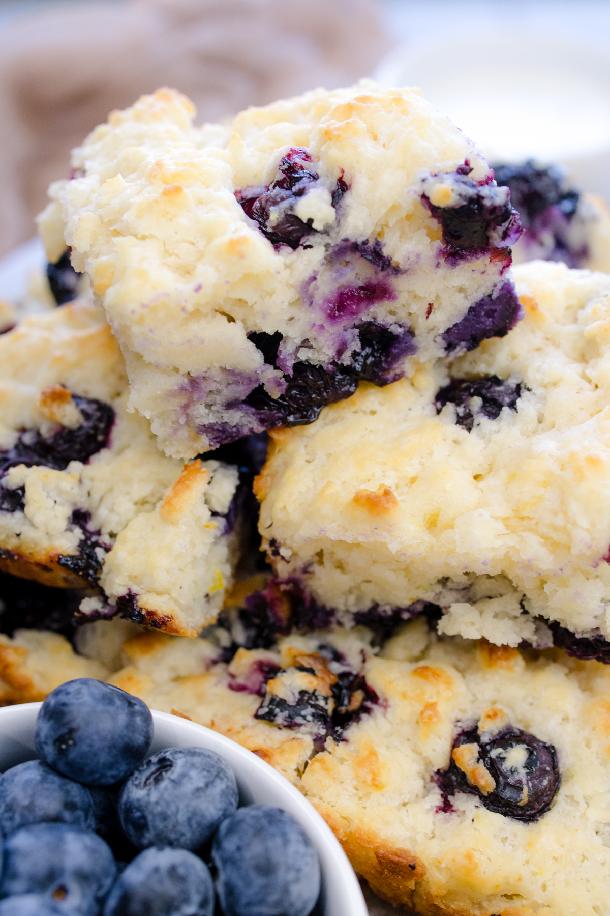 Angled view of Blueberry Biscuits stacked on top of each other next to blueberries.