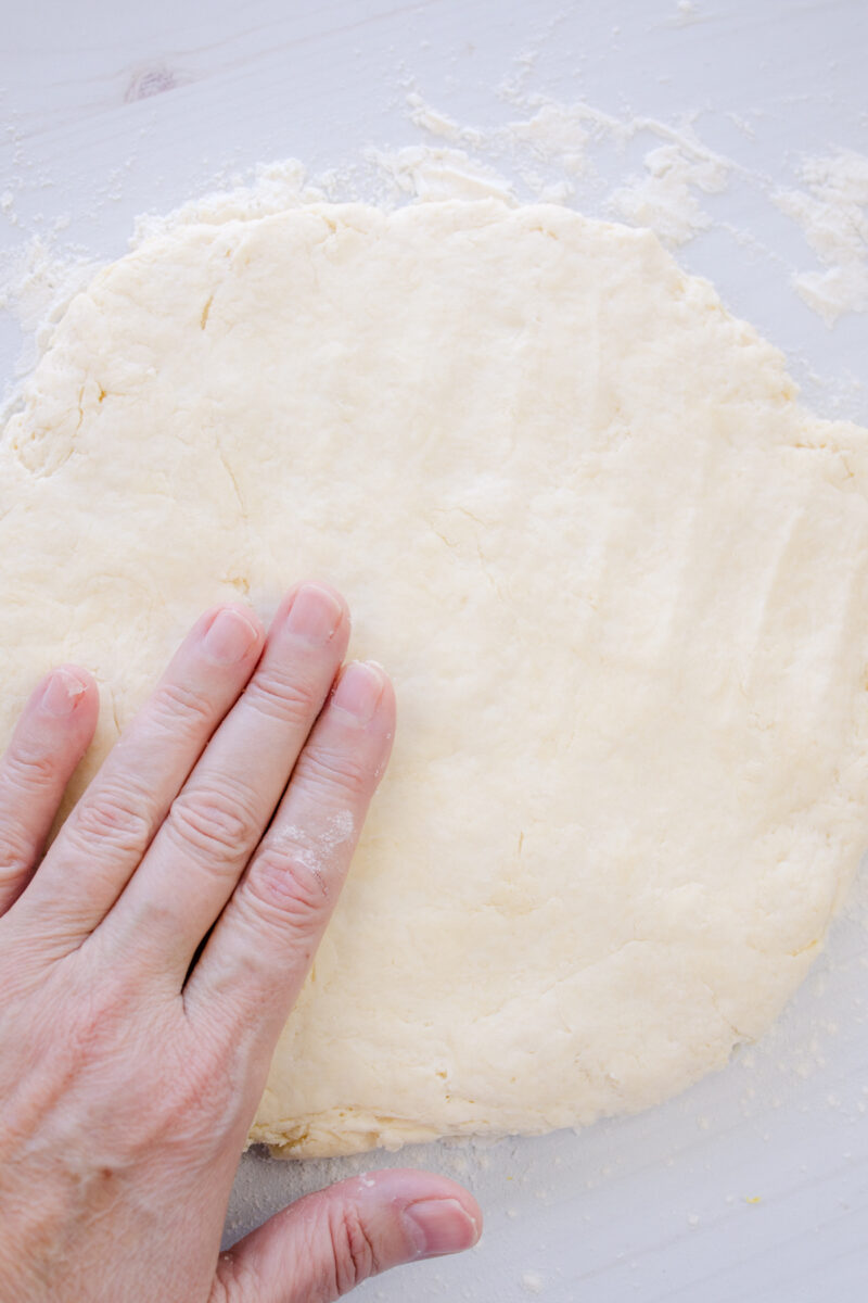 Overhead view of biscuit dough being flattened on a surface.