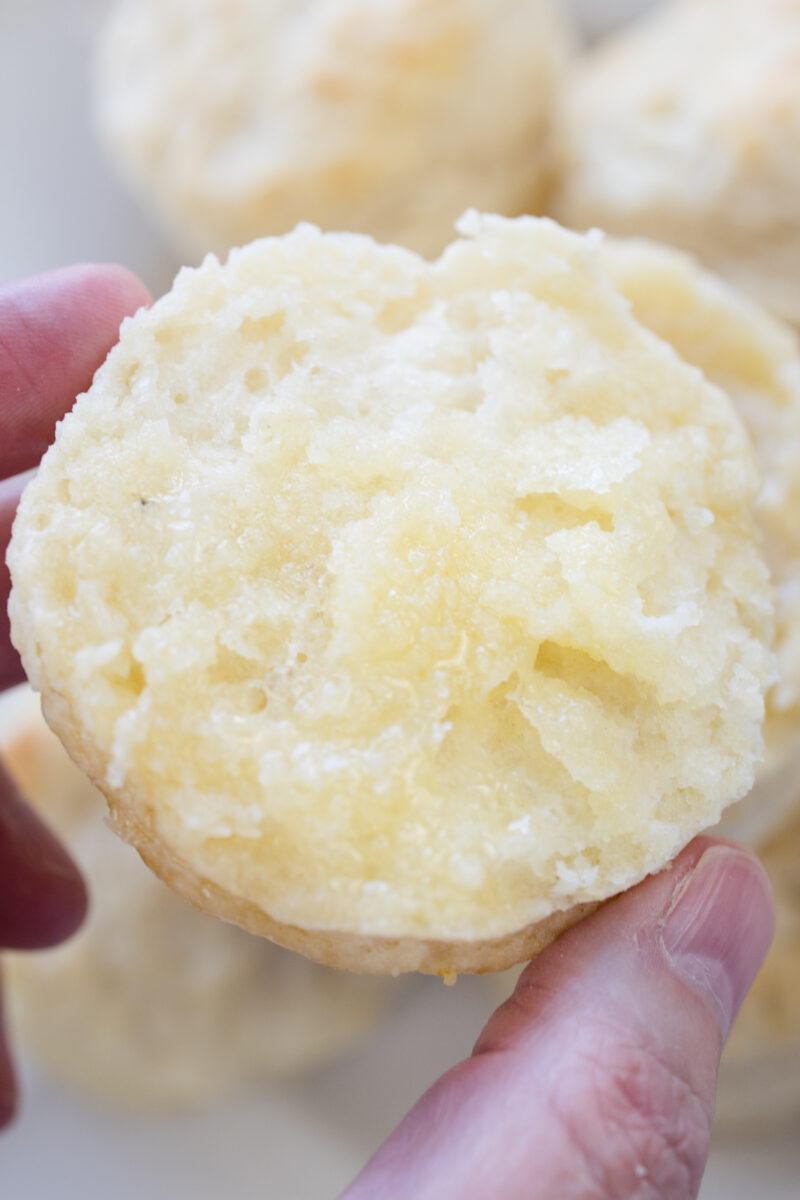 Close view of a hand holding a sliced half of a buttermilk biscuit.