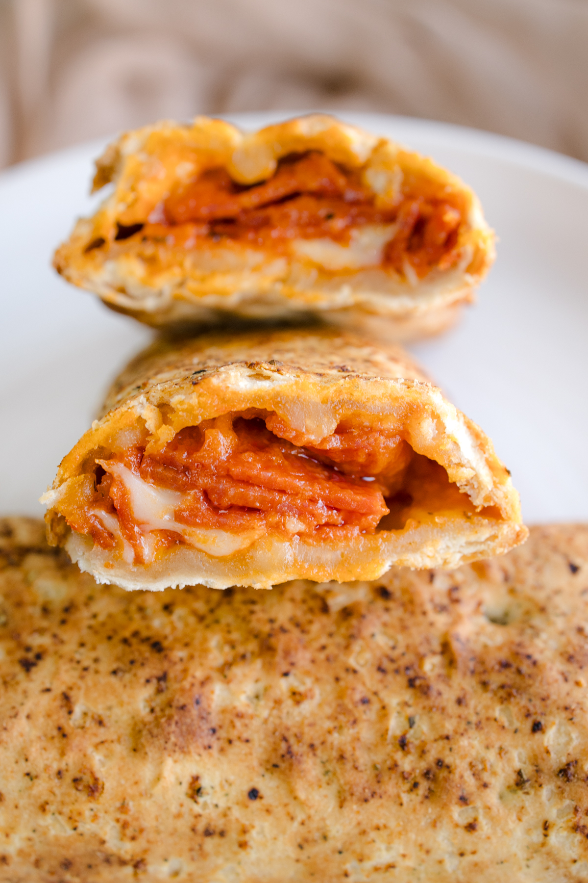 Close up view of a Hot Pocket sliced in half to reveal the middle, on a white plate.