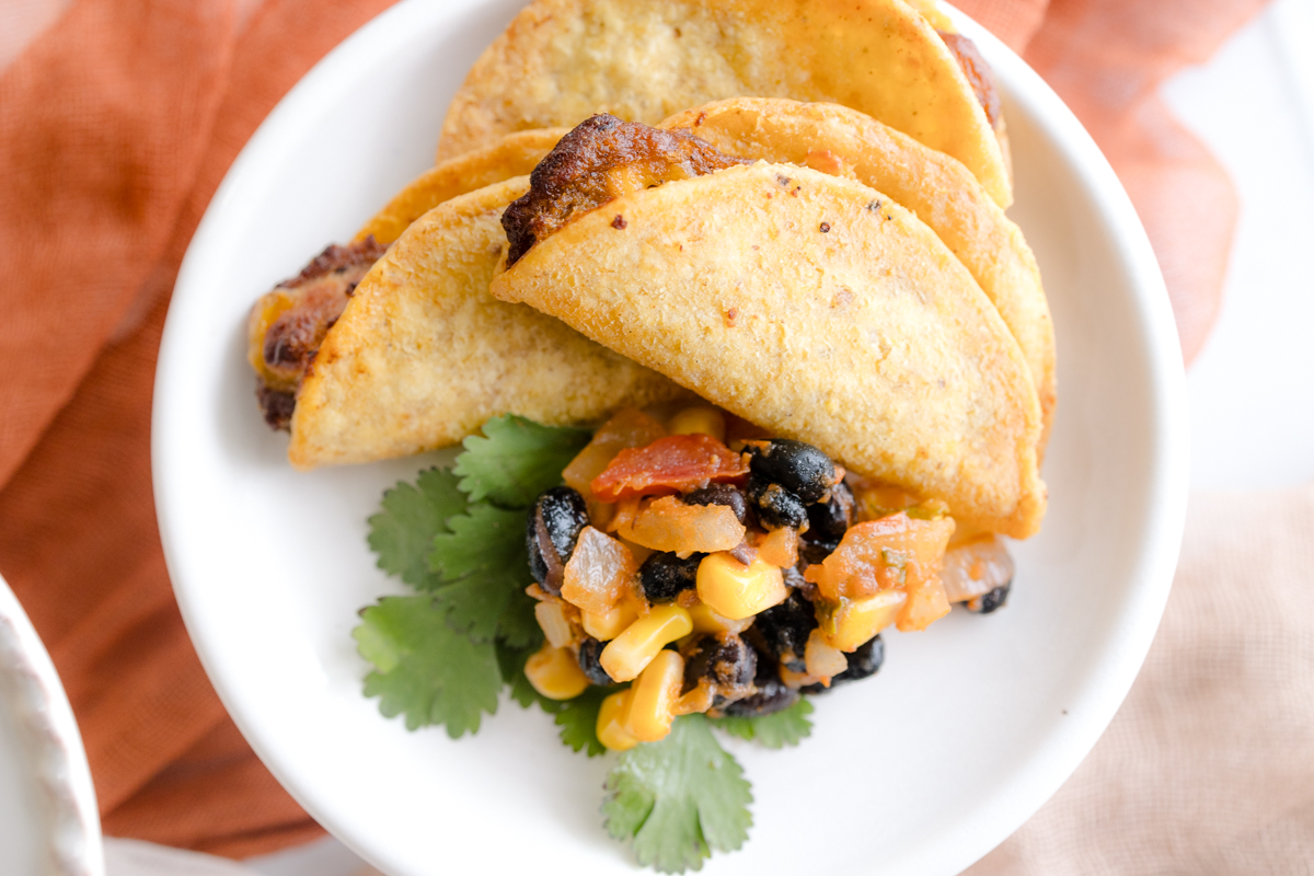Overhead view of a small plate with a few mini tacos on it with some salsa and cilantro.