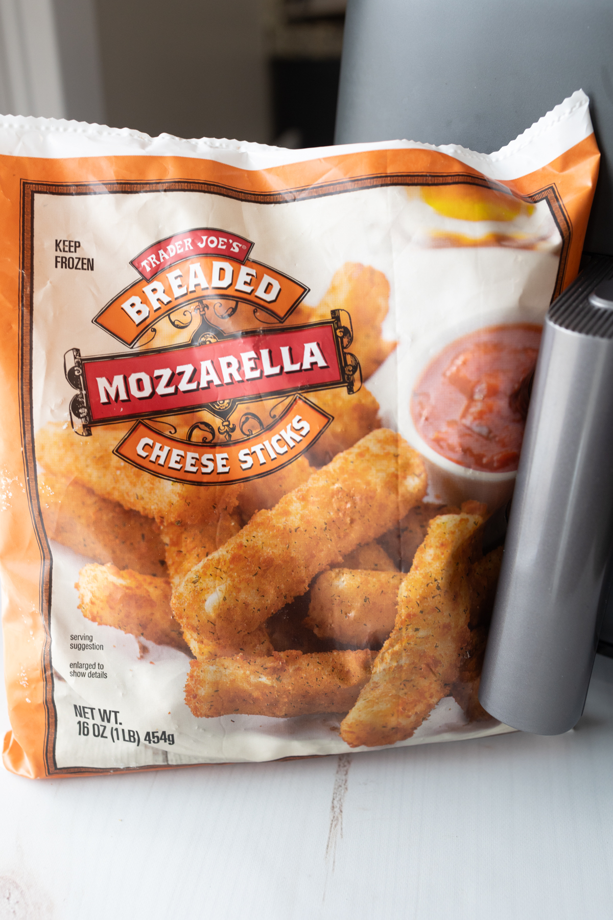 A bag of Trader Joe's Mozzarella Sticks in front of an air fryer.
