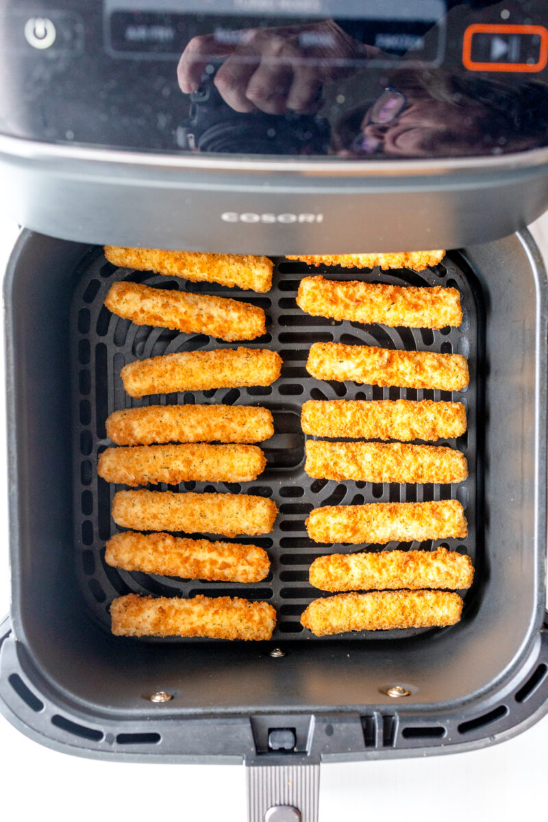 Overhead view of uncooked mozzarella sticks in an air fryer basket.