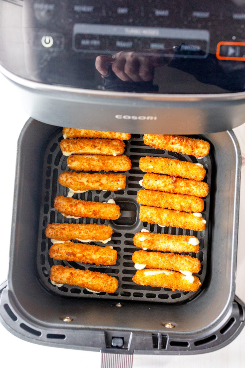 Overhead view of cooked mozzarella sticks in an air fryer basket.