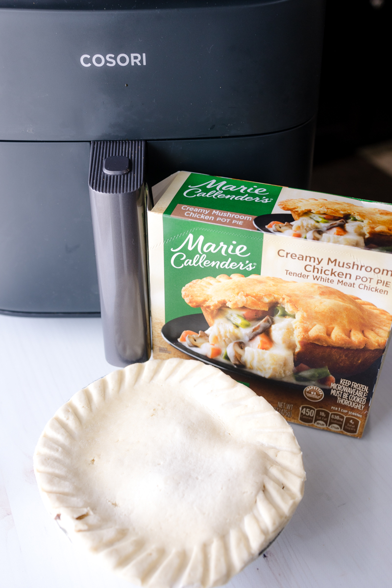 Angled view of an uncooked pot pie in front of its packaging and an air fryer.