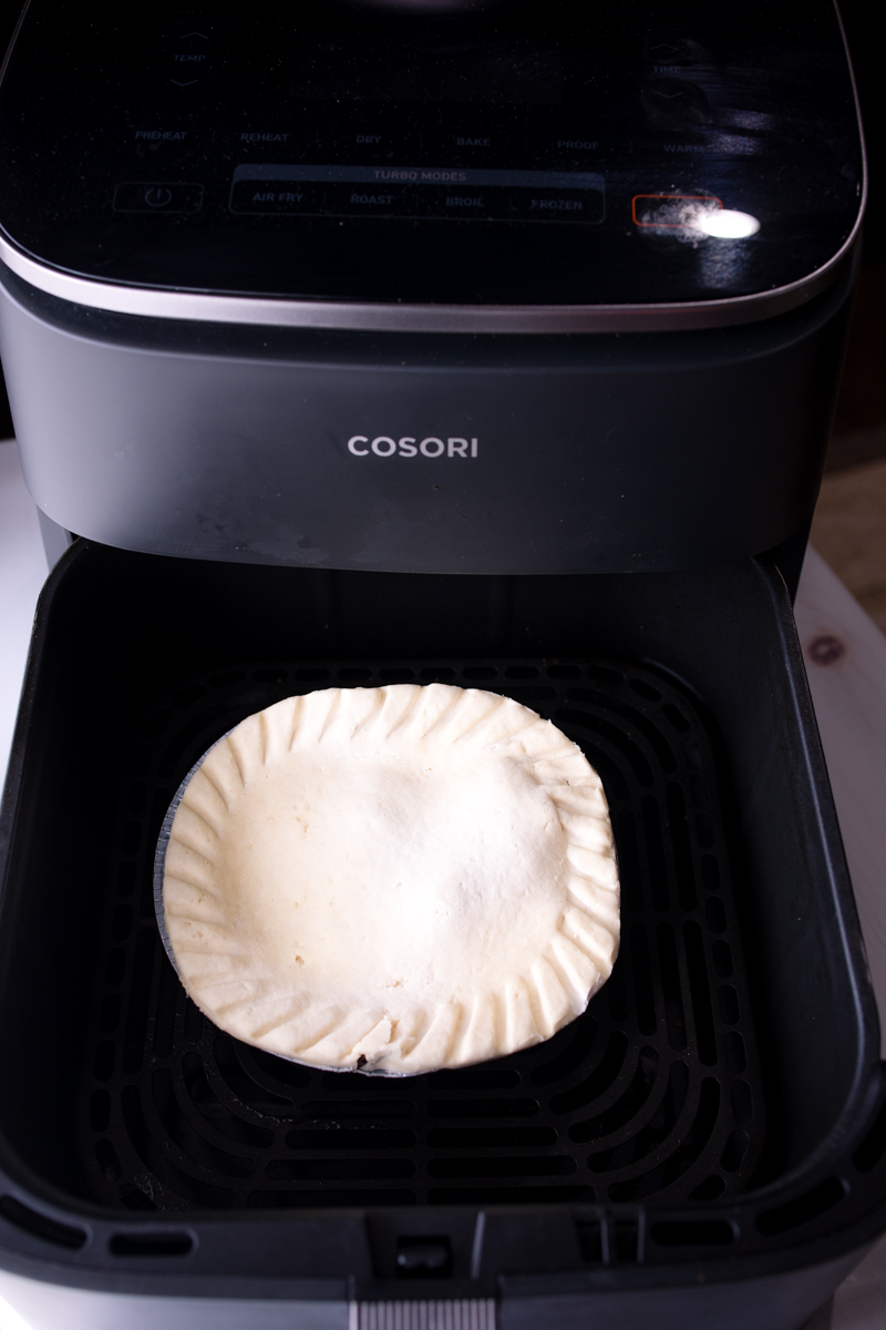 Angled view of an uncooked pot pie in an air fryer basket.