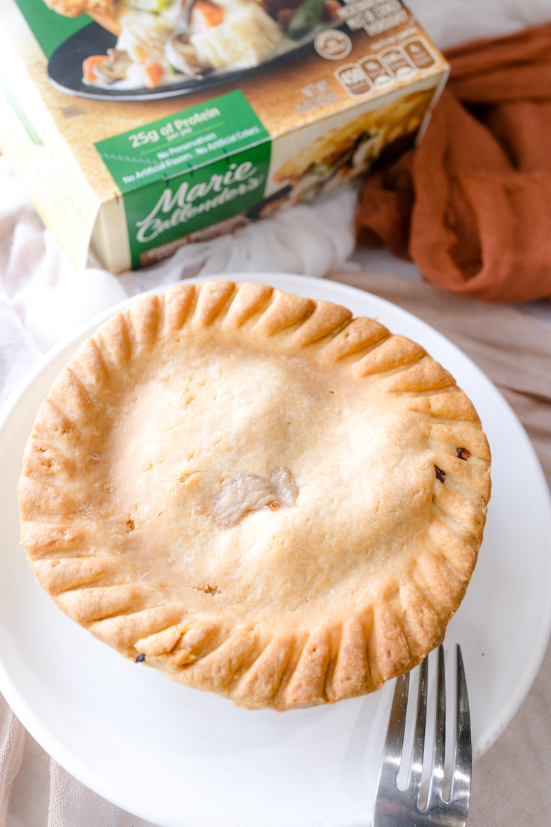 Angled view of a pot pie on a white plate, in front of its packaging.