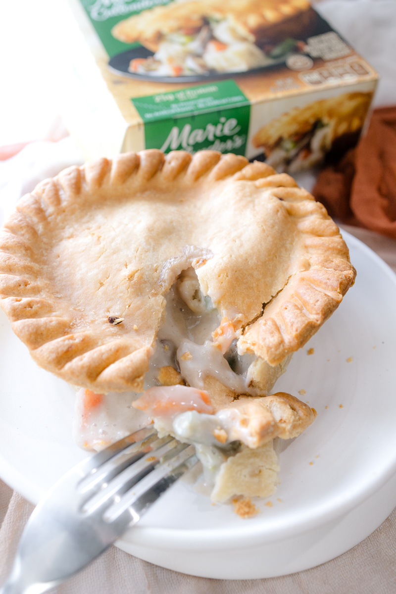 Angled view of a pot pie on a white plate, split open to reveal the filling. It is in front of its packaging.