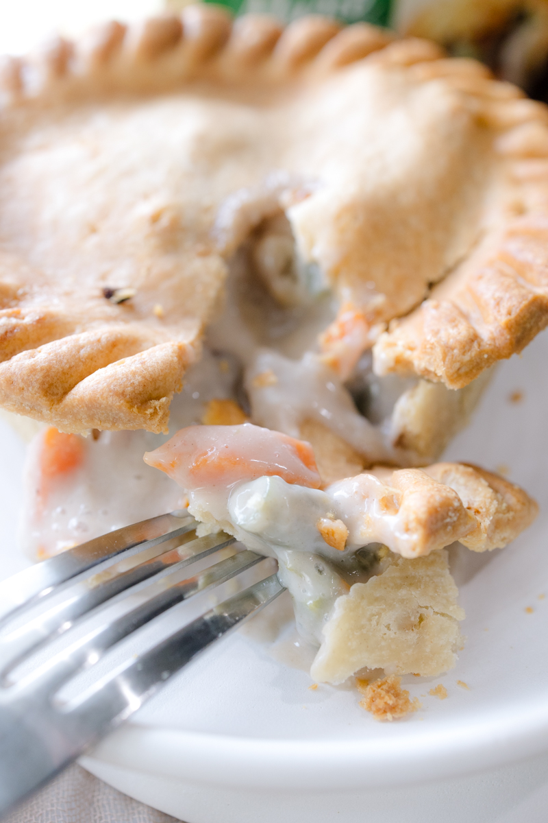 Close up angled view of a pot pie on a white plate, split open to reveal the filling.
