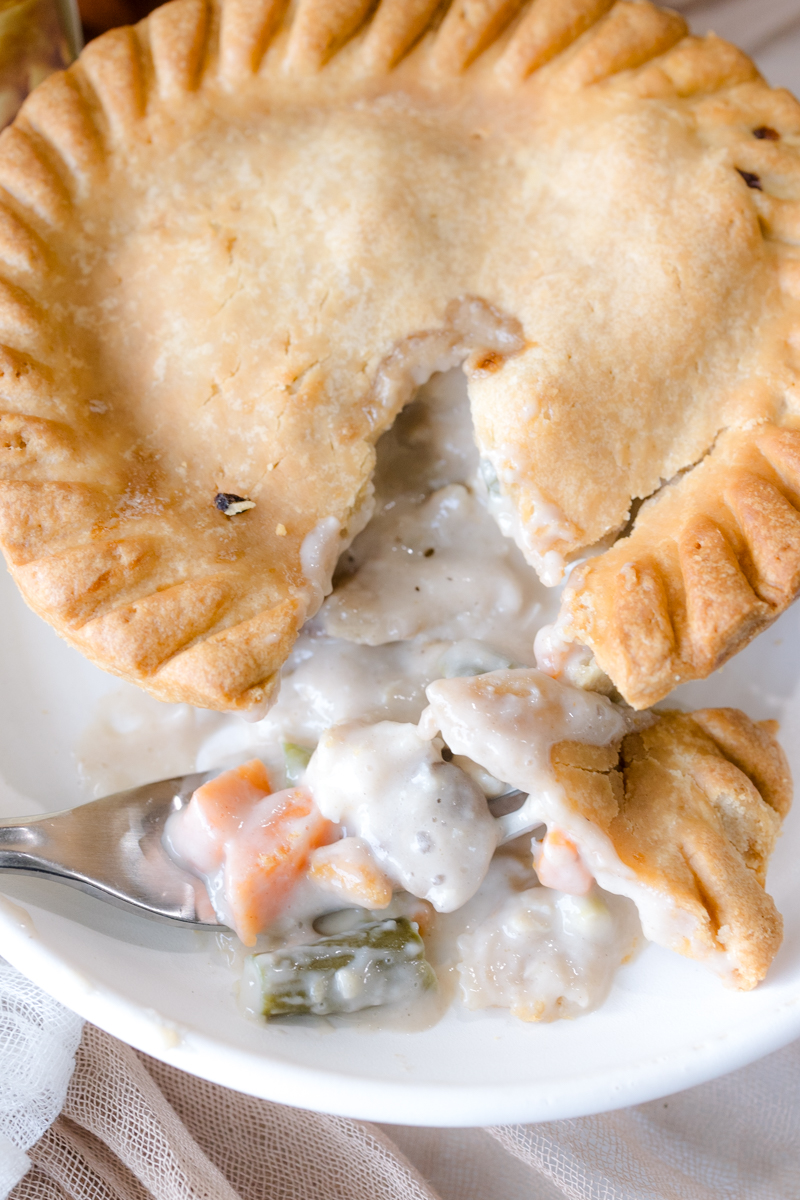 Close up angled view of a pot pie on a white plate, split open to reveal the filling.