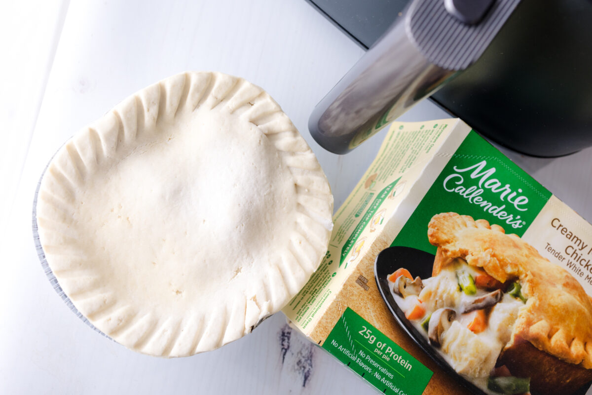 Overhead view of an uncooked pot pie beside its packaging and an air fryer.