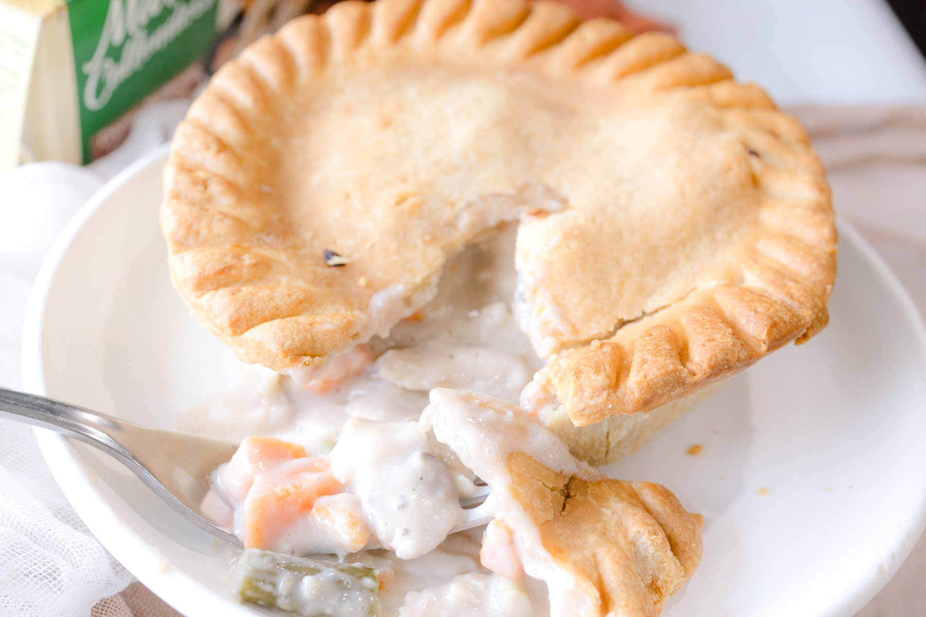 Close up angled view of a pot pie on a white plate, split open to reveal the filling.