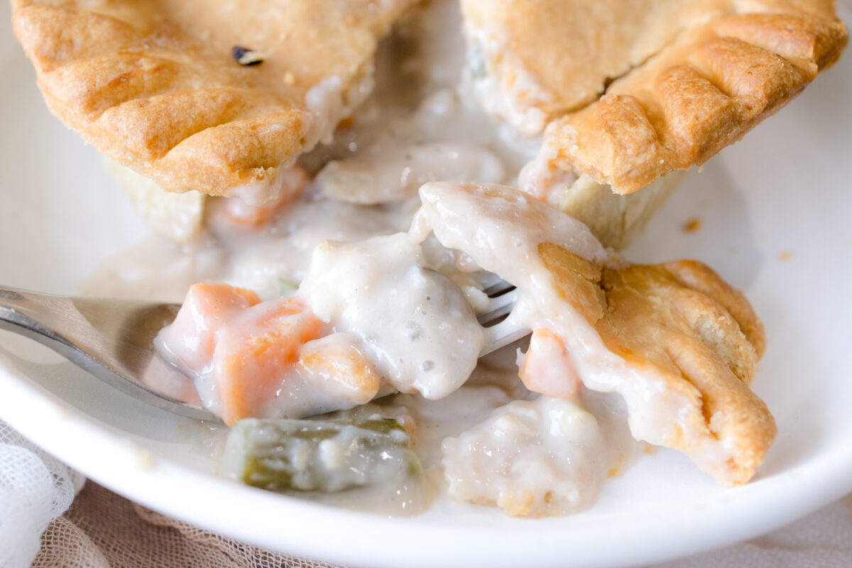 Close up overhead view of a pot pie on a white plate, split open to reveal the filling.
